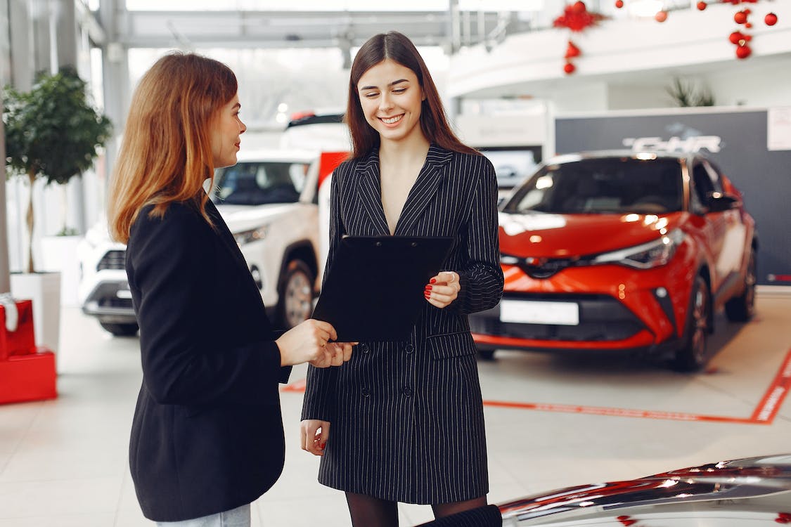 Two women standing holding a document in a car showroom