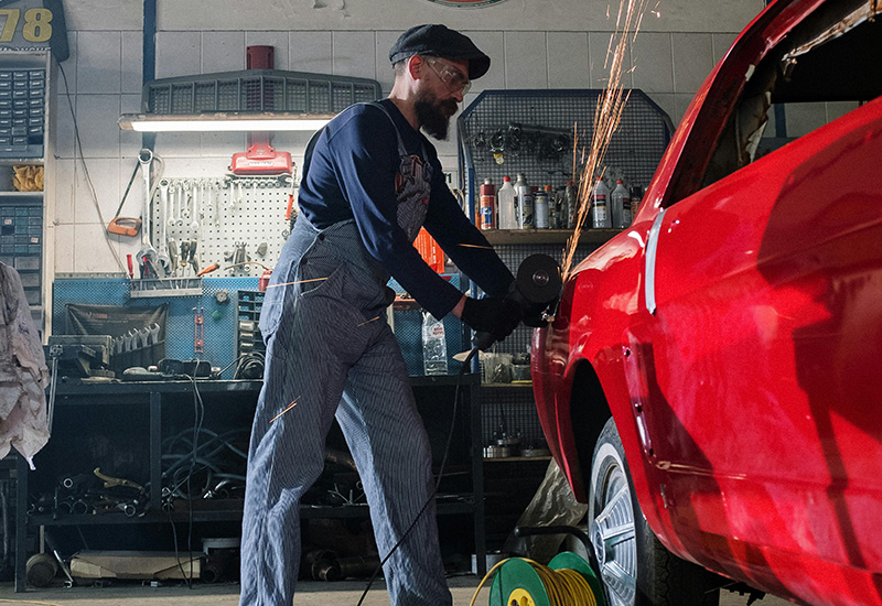 Sparks file as a mand grinds on the exterior of a red vehicle with a power tool