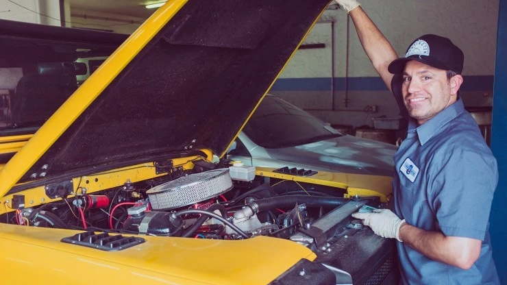 Man holding the hood of a yellow car and smiling