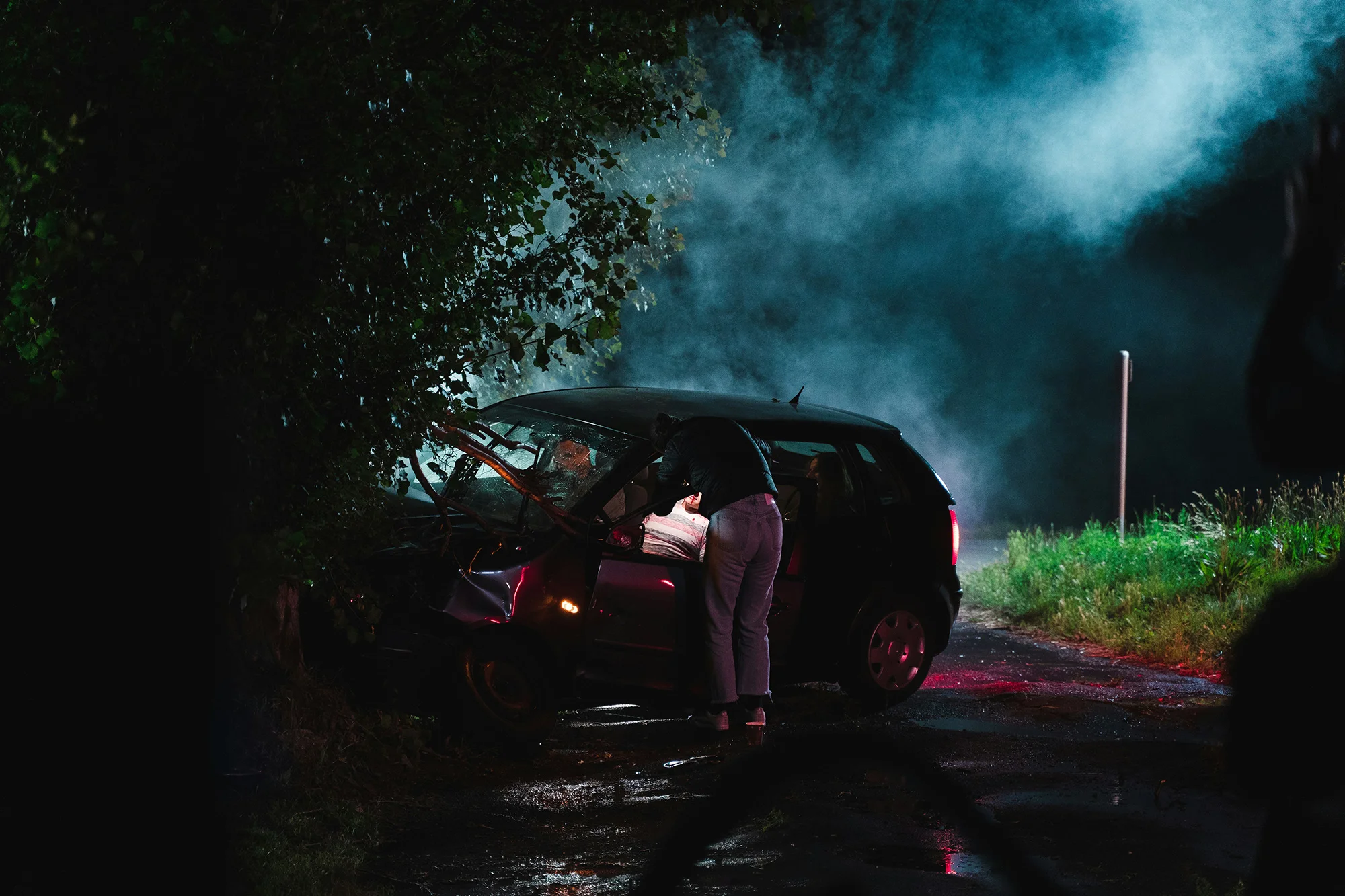 Car crashed into a tree at night with a person looking into the front seats