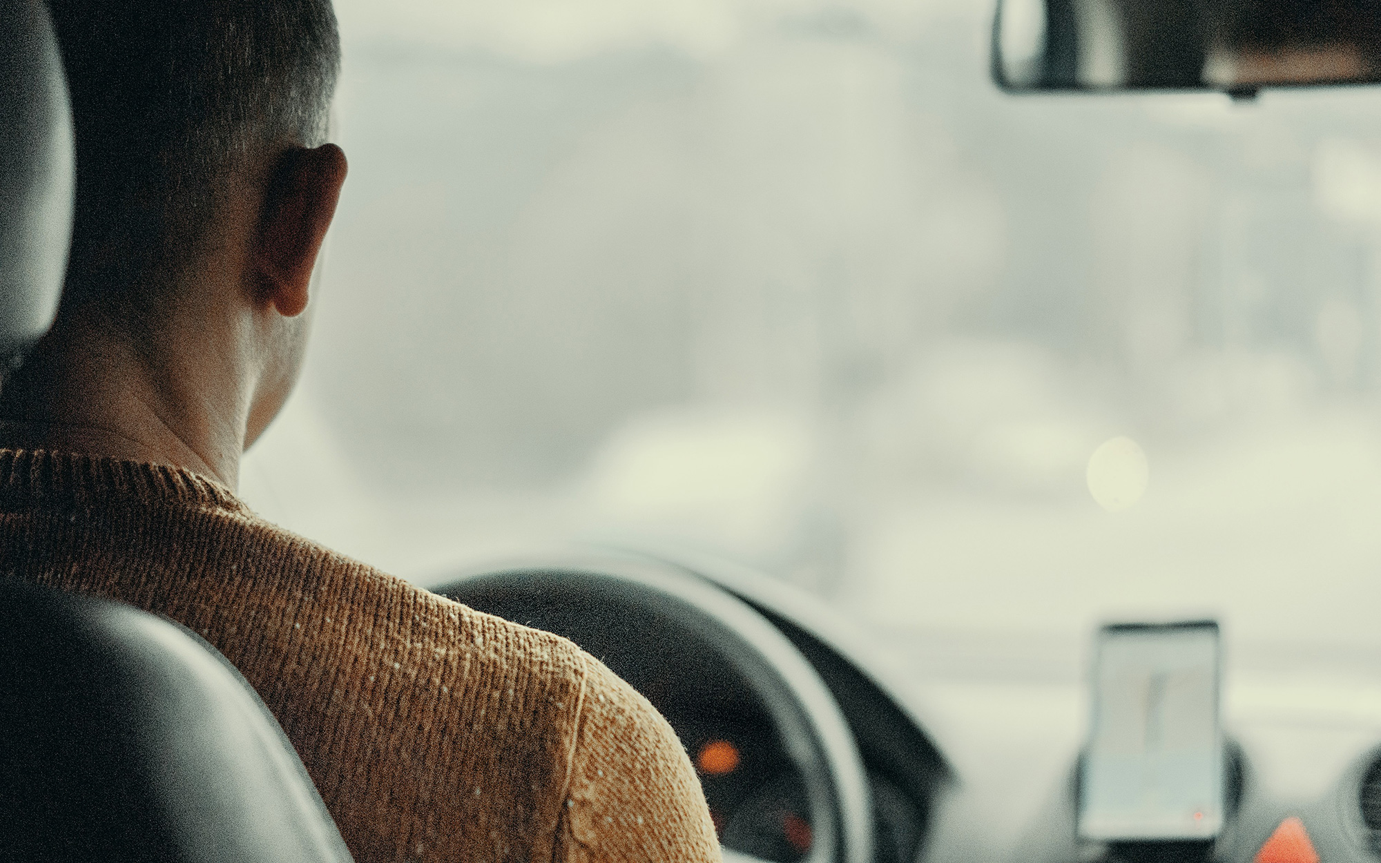 Back of man sitting at the steering wheel of a car.