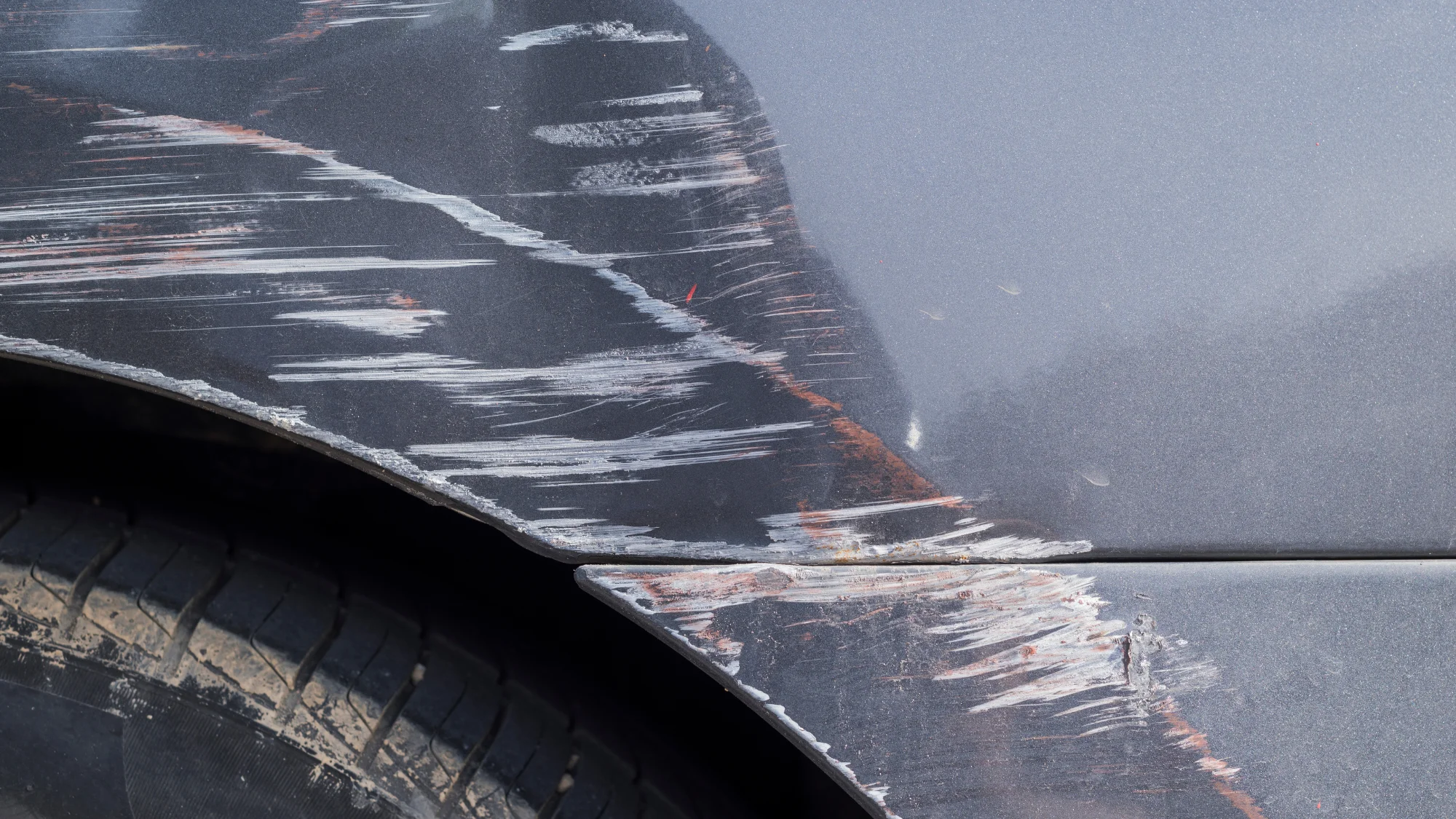 A close up of a grey car fender that has been severely scratched.