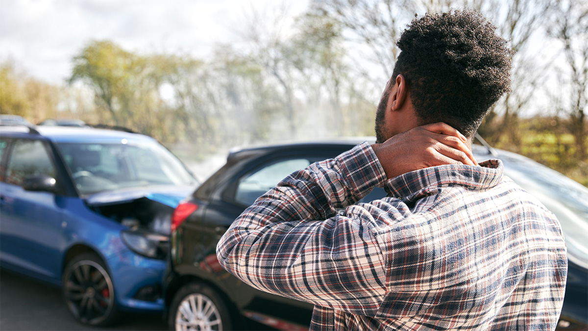 A man rubs his neck while looking at an accident where a car has been rear ended