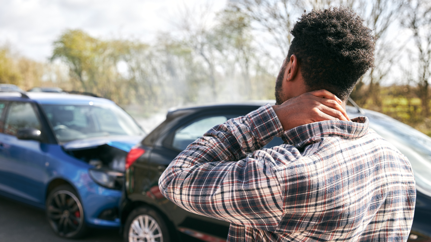 A man rubs his neck while looking at an accident where a car has been rear ended.