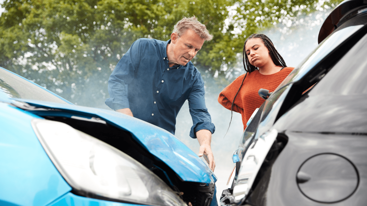 Two people examine their cars after an accident where one car was rear ended.