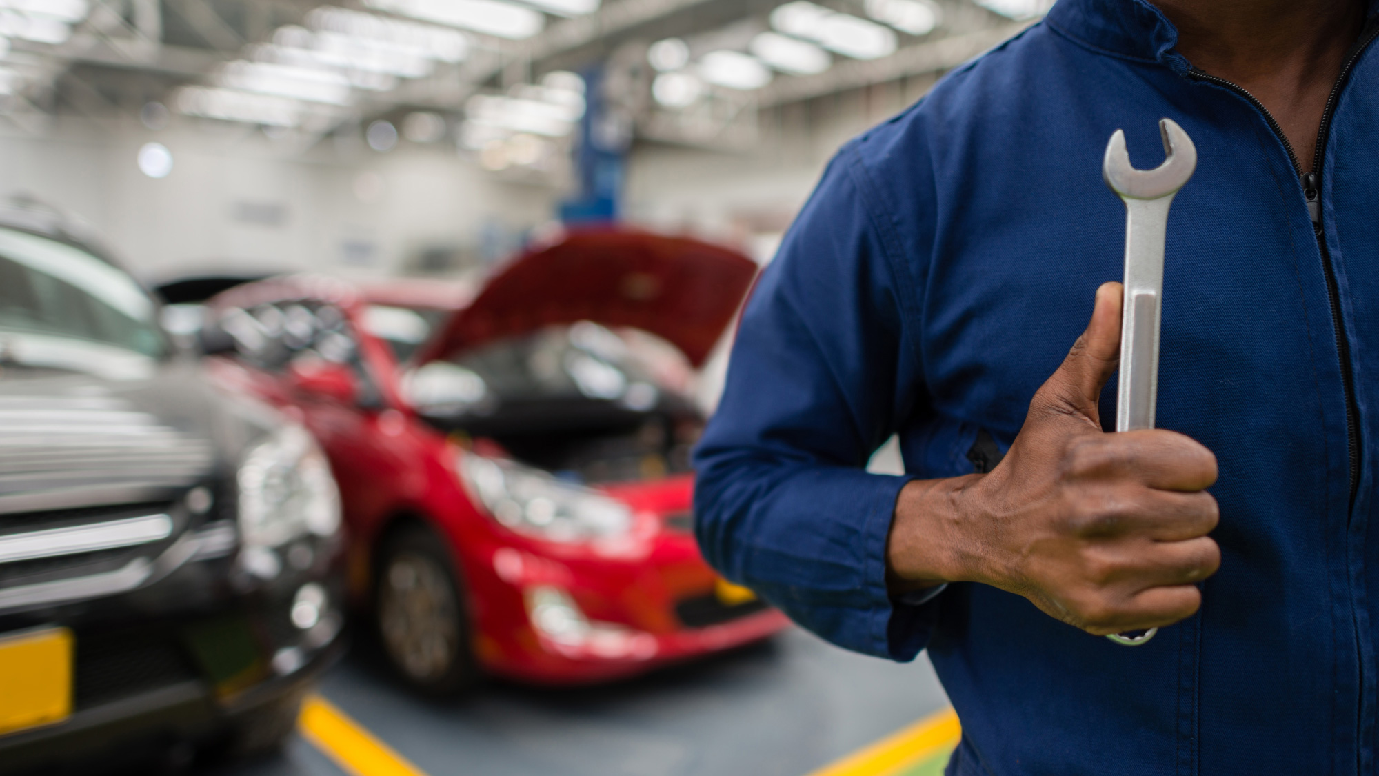 A man in a mechanics shop wearing a jumpsuit holds a wrench