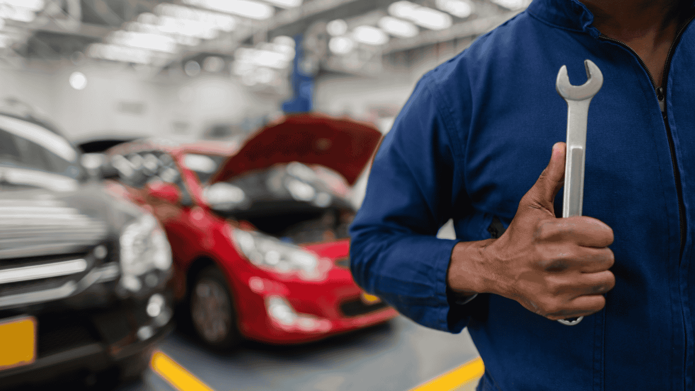 A man in a mechanic’s shop wearing a jumpsuit holds a wrench.