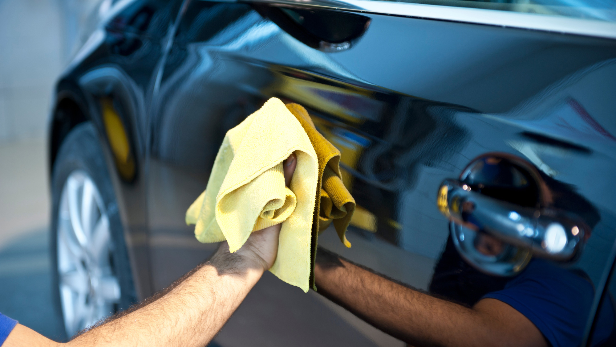 A man uses a microfiber cloth to clean the side of his car