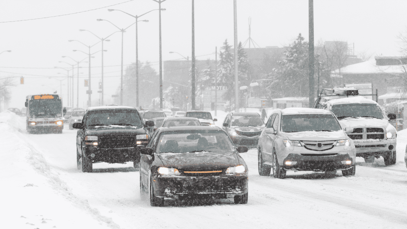 A snowy road in winter with many cars driving on it.