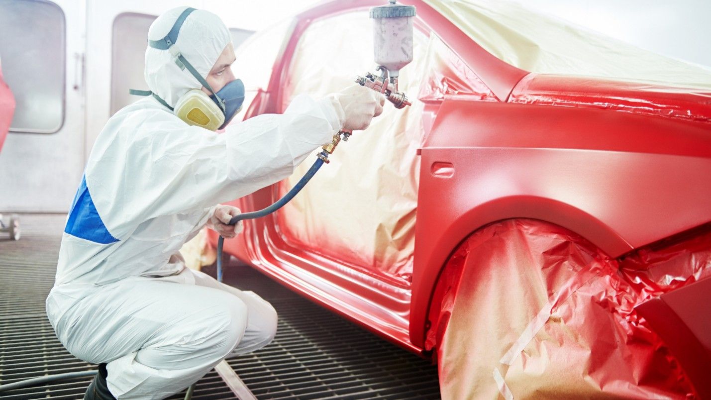 A professional auto painter sprays red paint on a car panel.
