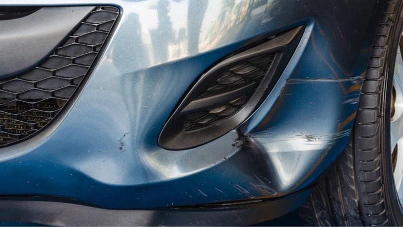 A close up view of a blue car bumper with a dent in it.