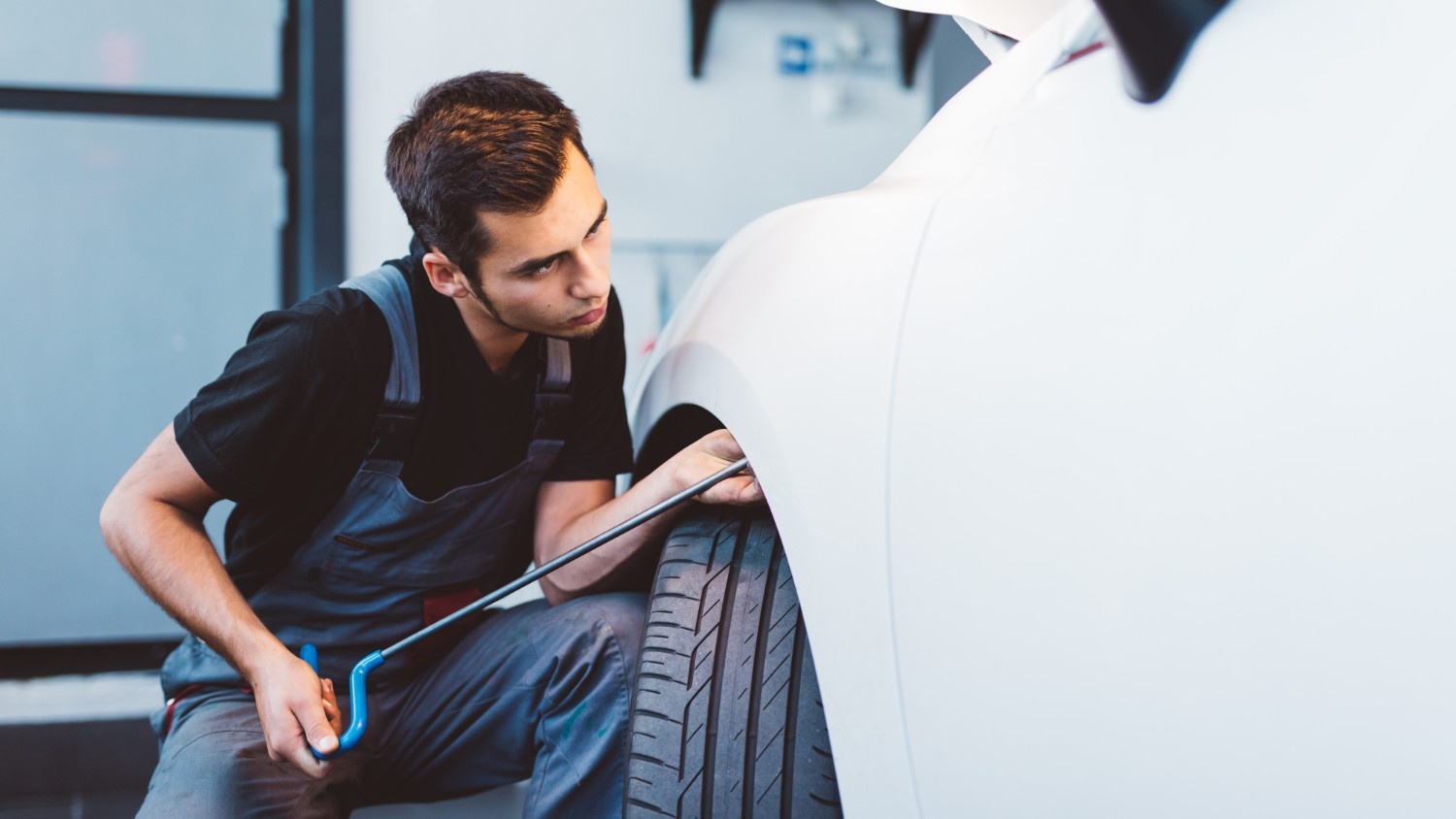 An auto body technician uses a tool to remove a dent on a white car.