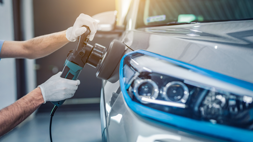 An auto technician buffs out scratches on a grey vehicle.