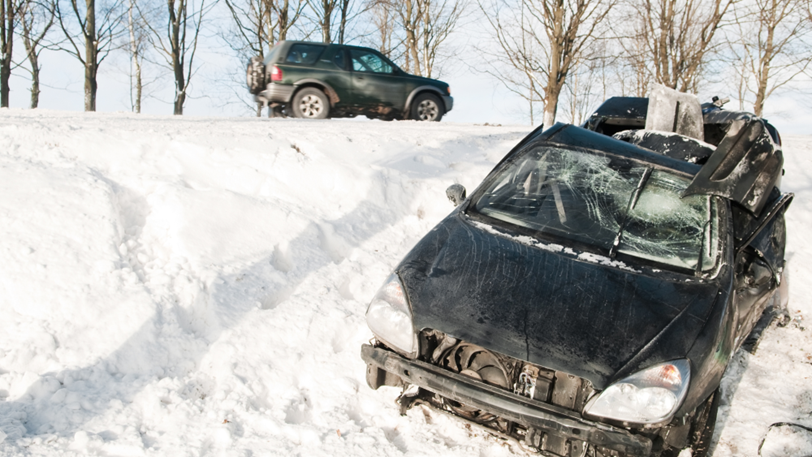 A crashed car is crumpled in a snowy ditch on the side of the road.