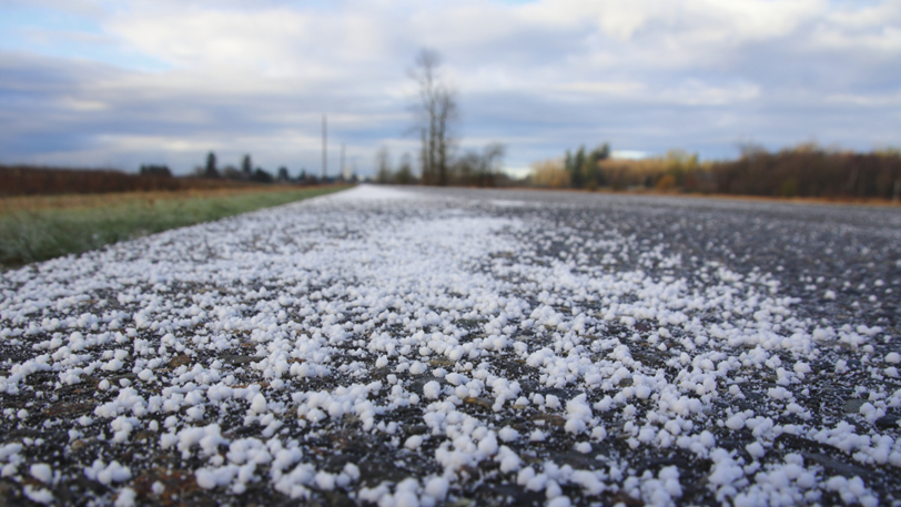 A paved road with large chunks of white road salt scattered across it.