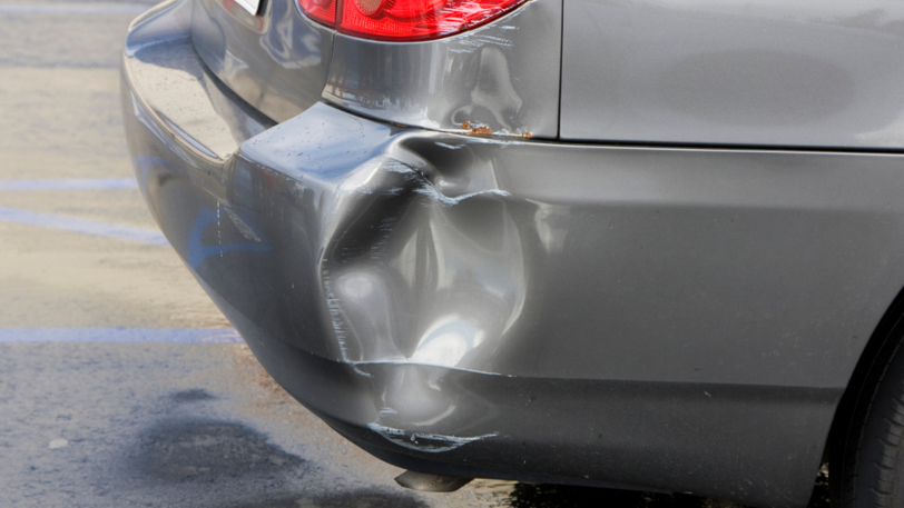 A grey colored car with a large dent on its’ right rear bumper after an accident.
